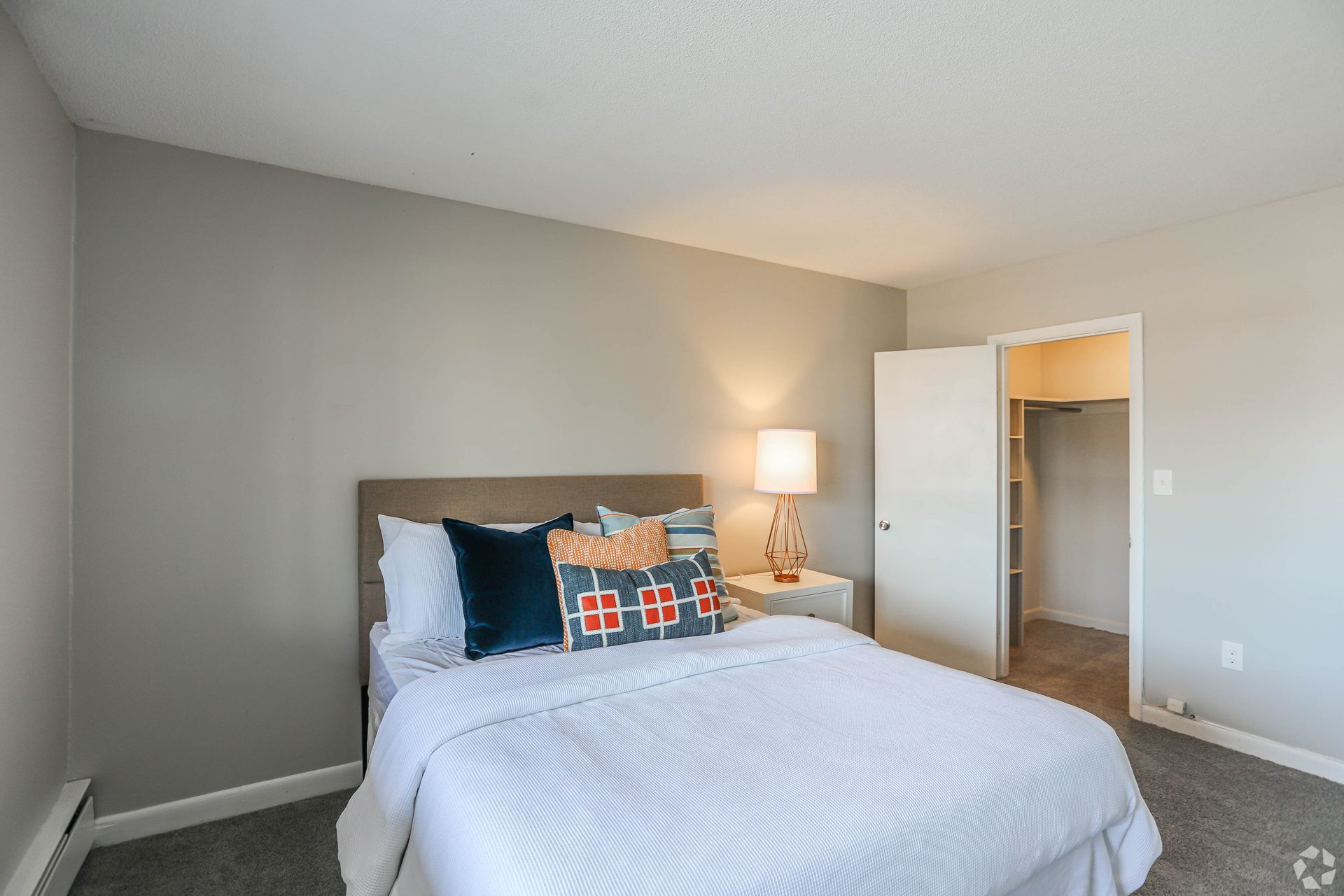 Bedroom with bed, pillows, nightstand, lamp, and open closet. Gray walls, white bedding, and carpet.