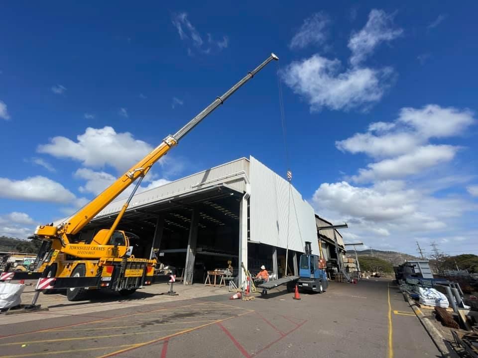 A Large Yellow Crane is Lifting a Large White Building — Northern Plumbing In Mount Louisa, QLD