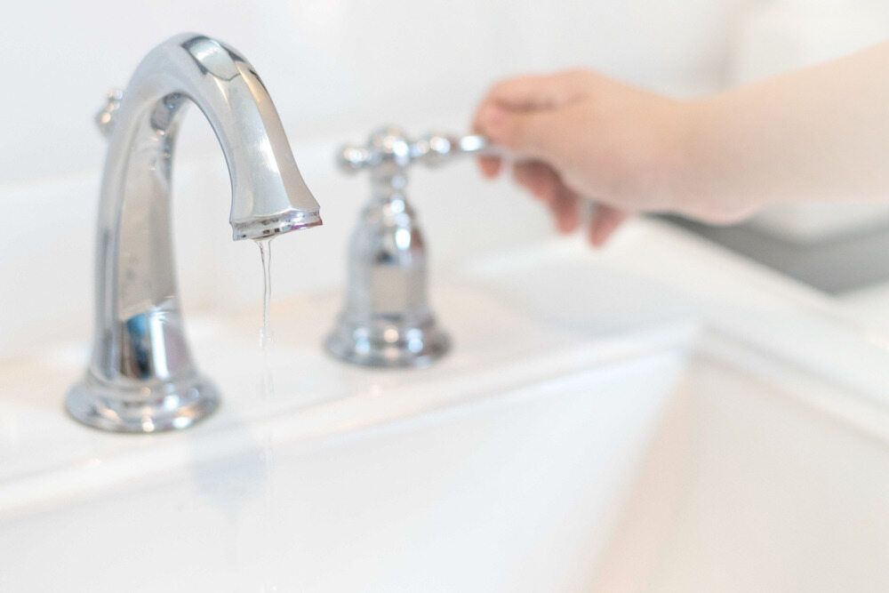 A Person is Turning on a Bathroom Sink Faucet — Northern Plumbing In Mount Louisa, QLD