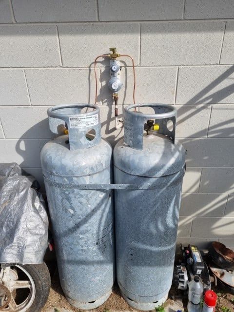 Two Gas Cylinders Are Sitting in Front of a Brick Wall — Northern Plumbing In Mount Louisa, QLD