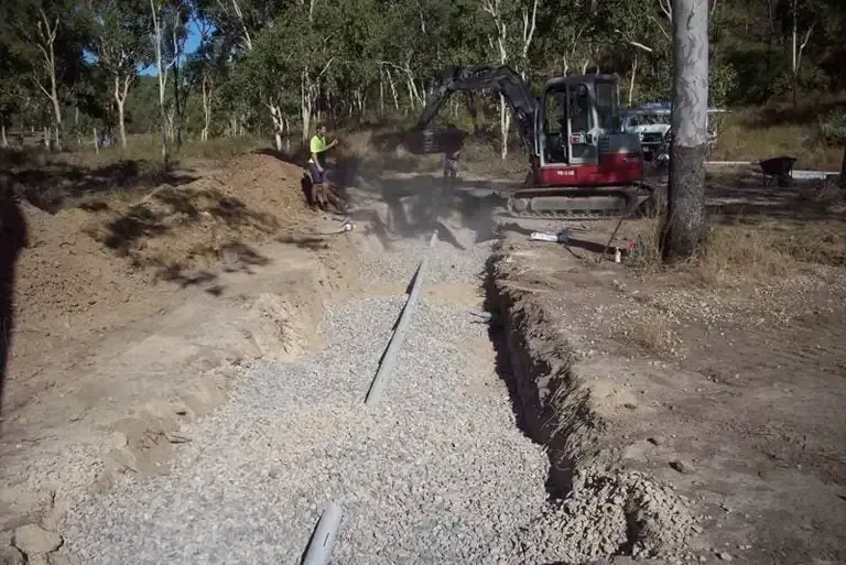 A Red Excavator is Digging a Trench in the Dirt — Northern Plumbing In Mount Louisa, QLD