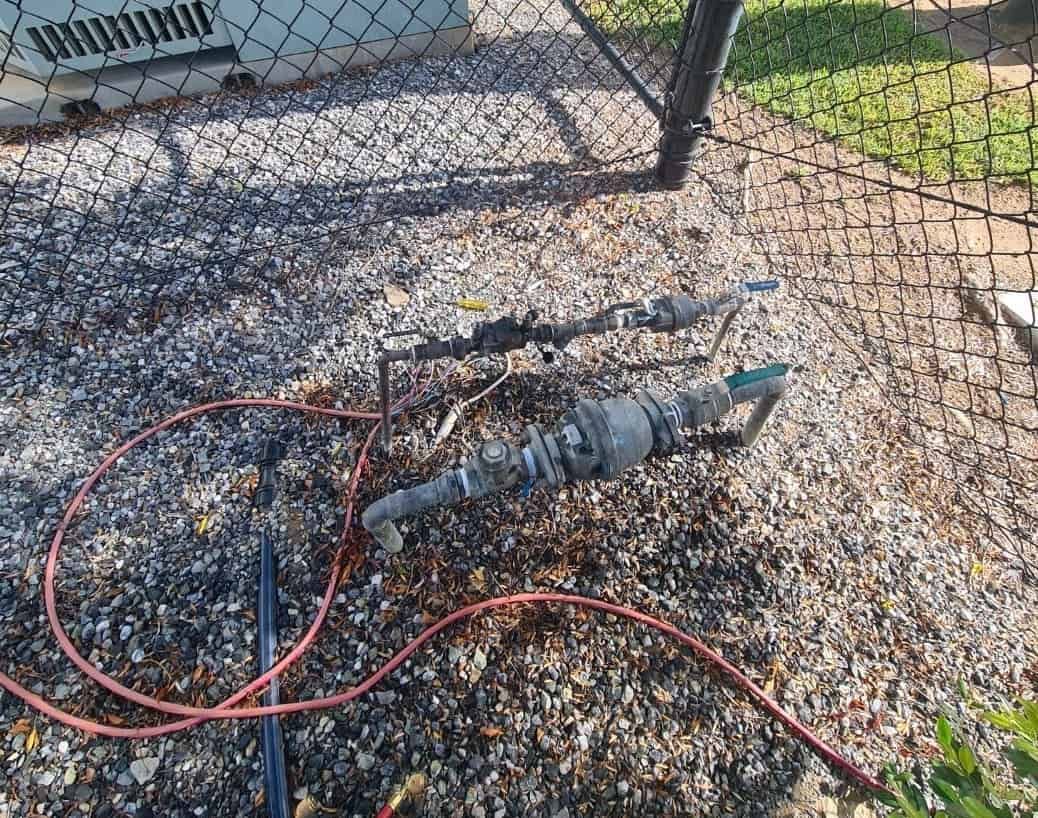 A Hose is Laying on the Ground Next to a Chain Link Fence — Northern Plumbing In Mount Louisa, QLD