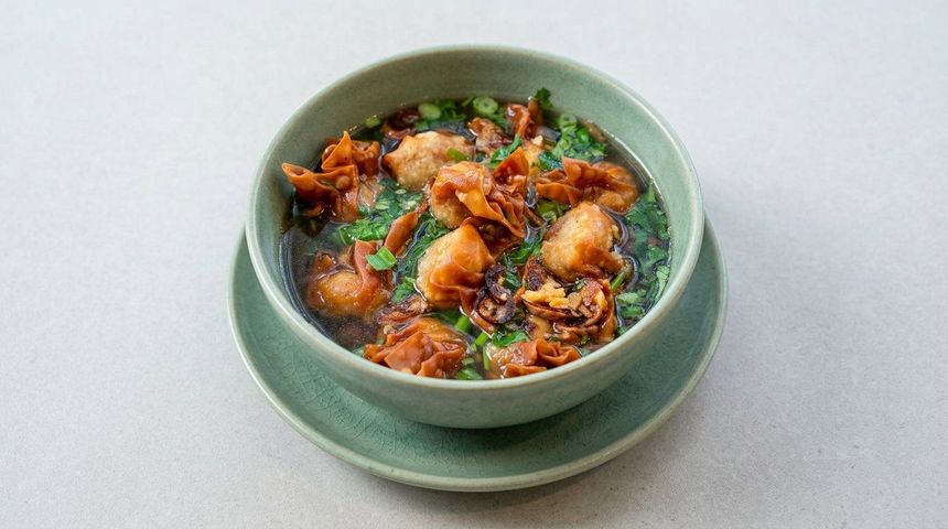 Green bowl of saucy fried food on a matching saucer against a light gray background
