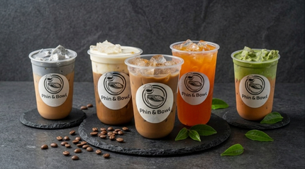 Five assorted iced coffee drinks in clear cups, lined up on a dark table with coffee beans and green leaves.