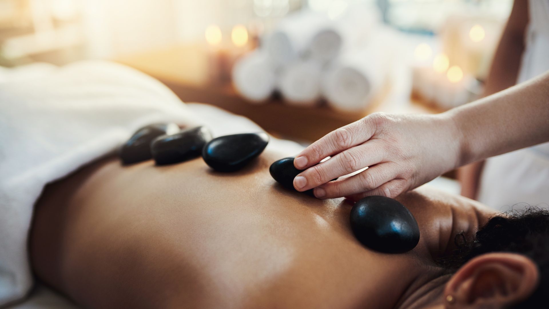 Hot stone massage on a person’s back, with a therapist’s hand placing smooth black stones