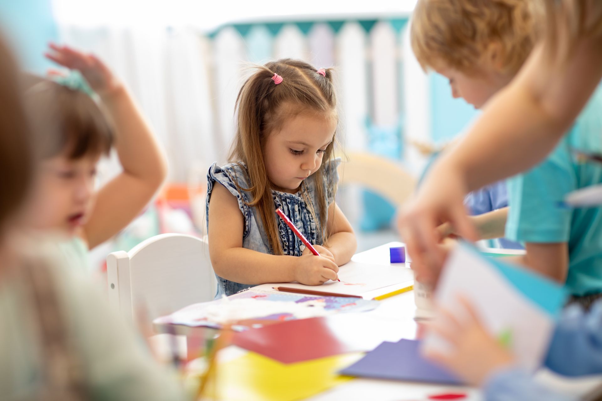 Child writing with a pencil at a desk in a classroom, focused and leaning over the paper.