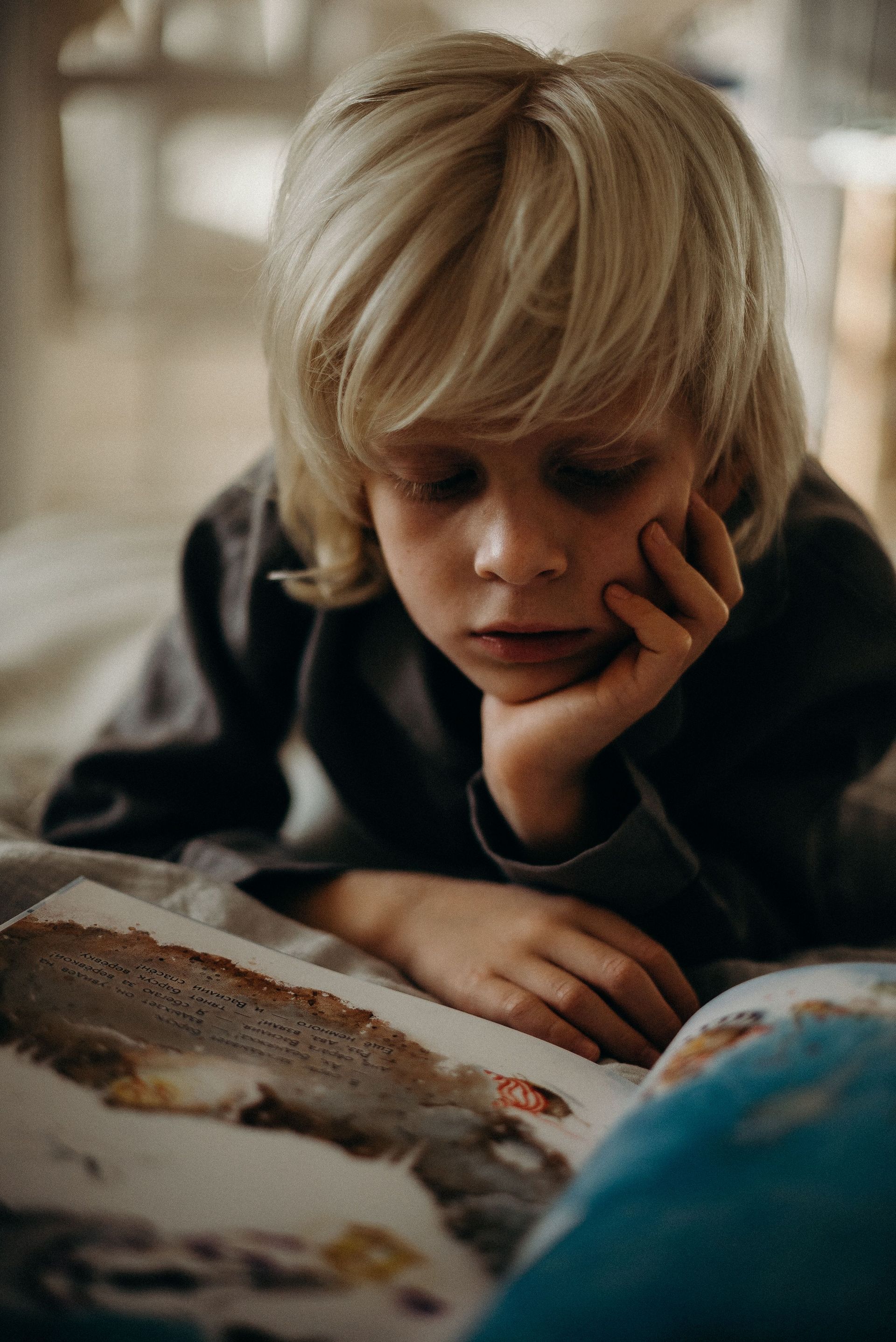 A child resting their head on their hand while reading, working harder than they should be to get through a page