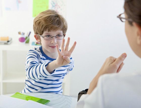 Child in striped shirt shows four fingers to a clinician during a consultation in a bright room.