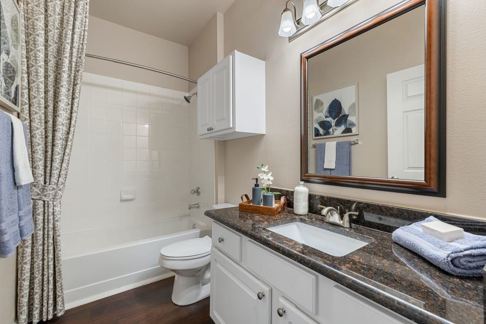 a bathroom with a sink, toilet, bathtub, and mirror at Marquis Carmel Commons in Charlotte, NC.