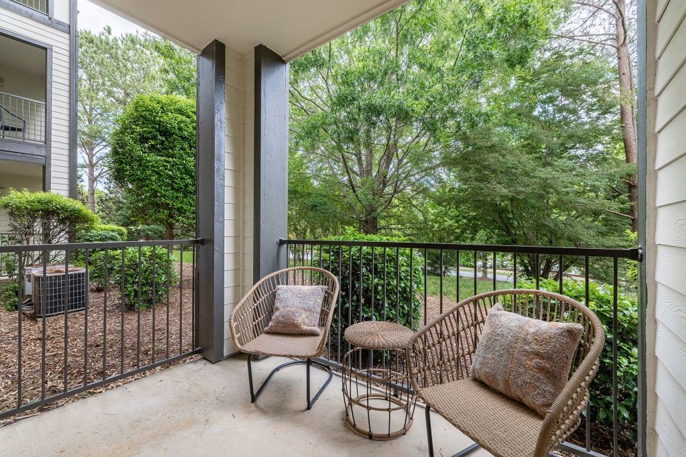 a balcony with two chairs and a table with trees in the background at Marquis Carmel Commons in Charlotte, NC.