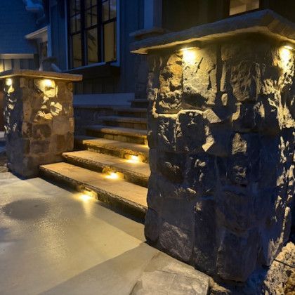 Stone pillars with lights frame illuminated steps leading to a building entrance at night.