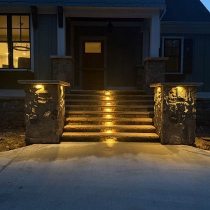 Stone steps with built-in lights leading to a house entrance at night. Pillars frame the steps.