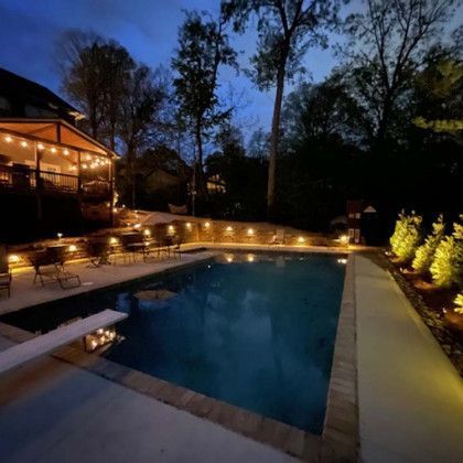 Nighttime view of a pool with surrounding lights and a deck in a backyard.
