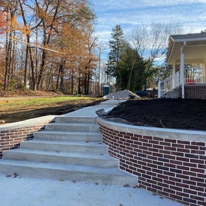 Concrete steps with brick retaining walls lead to a white porch with a view of fall foliage.