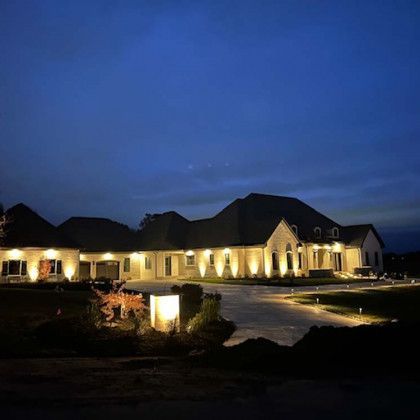 Large house illuminated at night with exterior lighting. Dark blue sky.