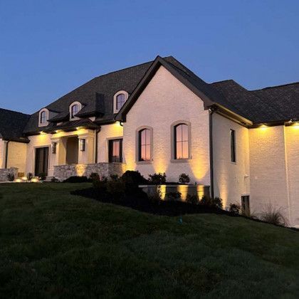 Exterior of a large, two-story white brick house at dusk, illuminated with warm lighting.
