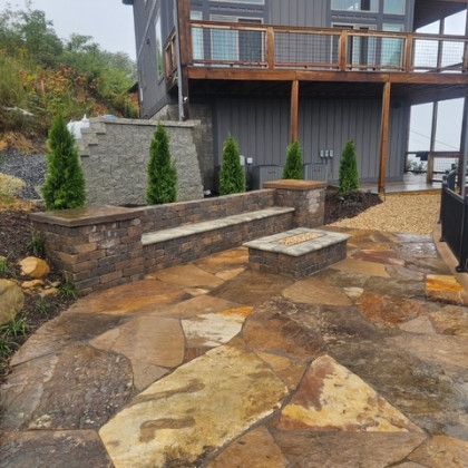 Outdoor patio with stone pavers, seating wall, and fire pit in front of a house.