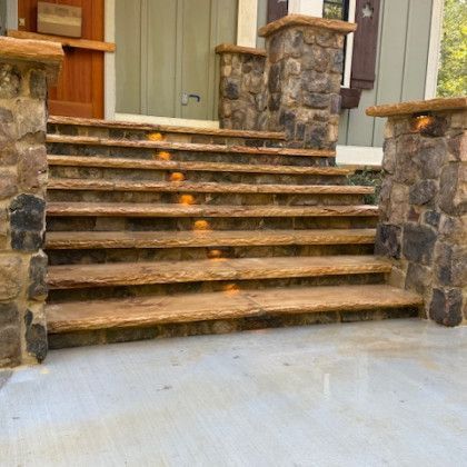Stone stairs leading to a front door, flanked by stone pillars. Embedded lights illuminate steps.