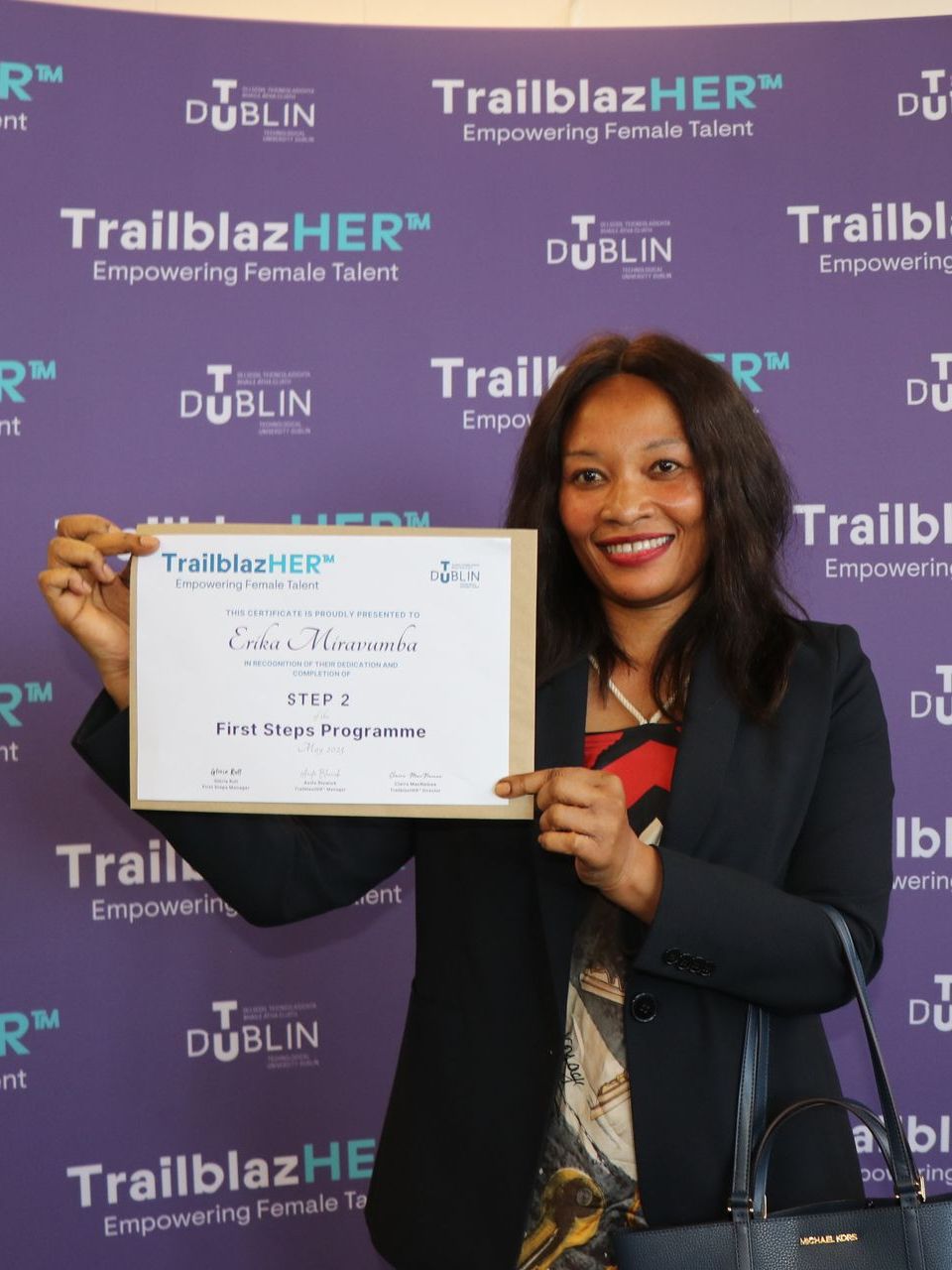 Woman holding a certificate in front of a TrailblazHER event backdrop