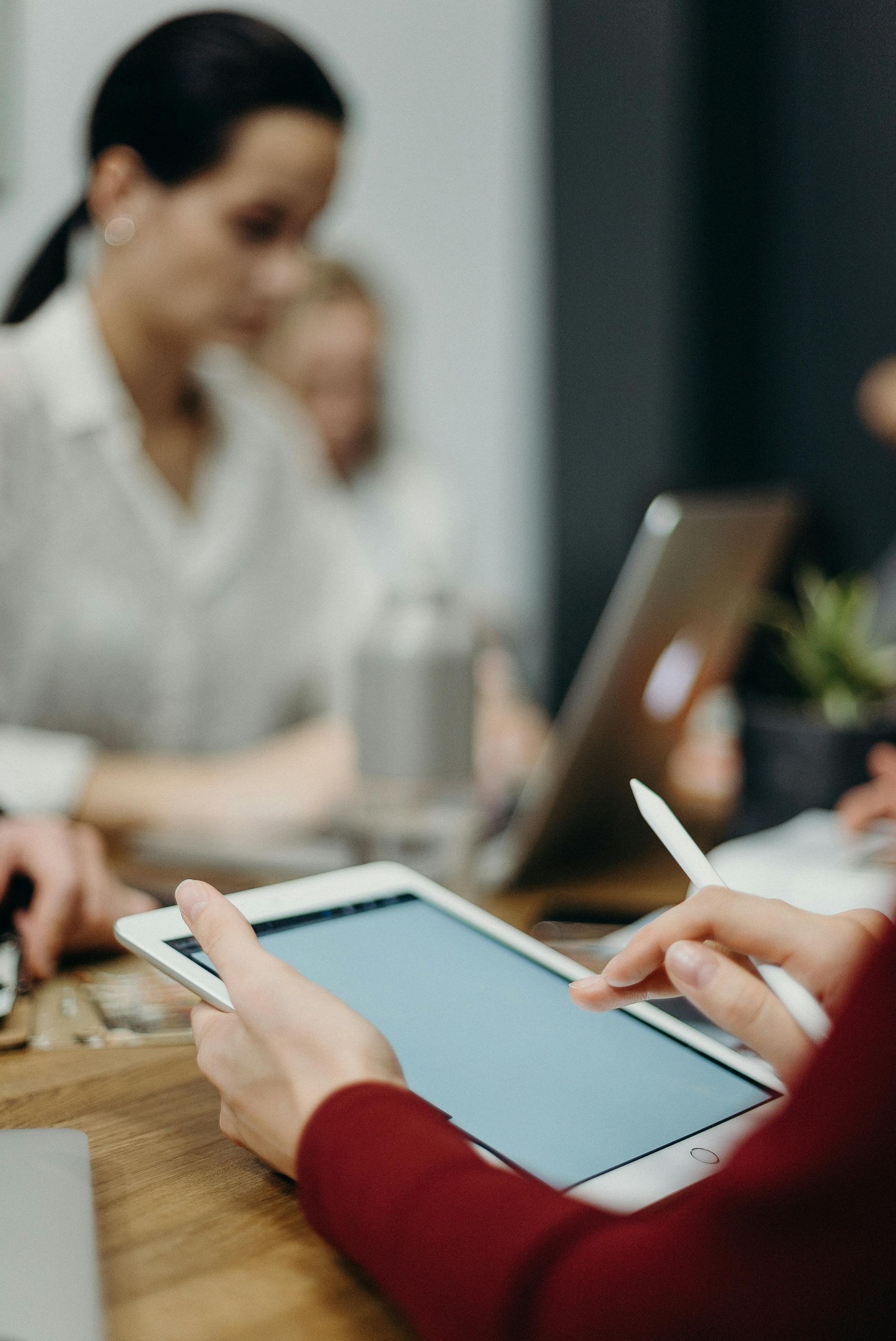 People using a tablet and laptop in a meeting at a wooden table