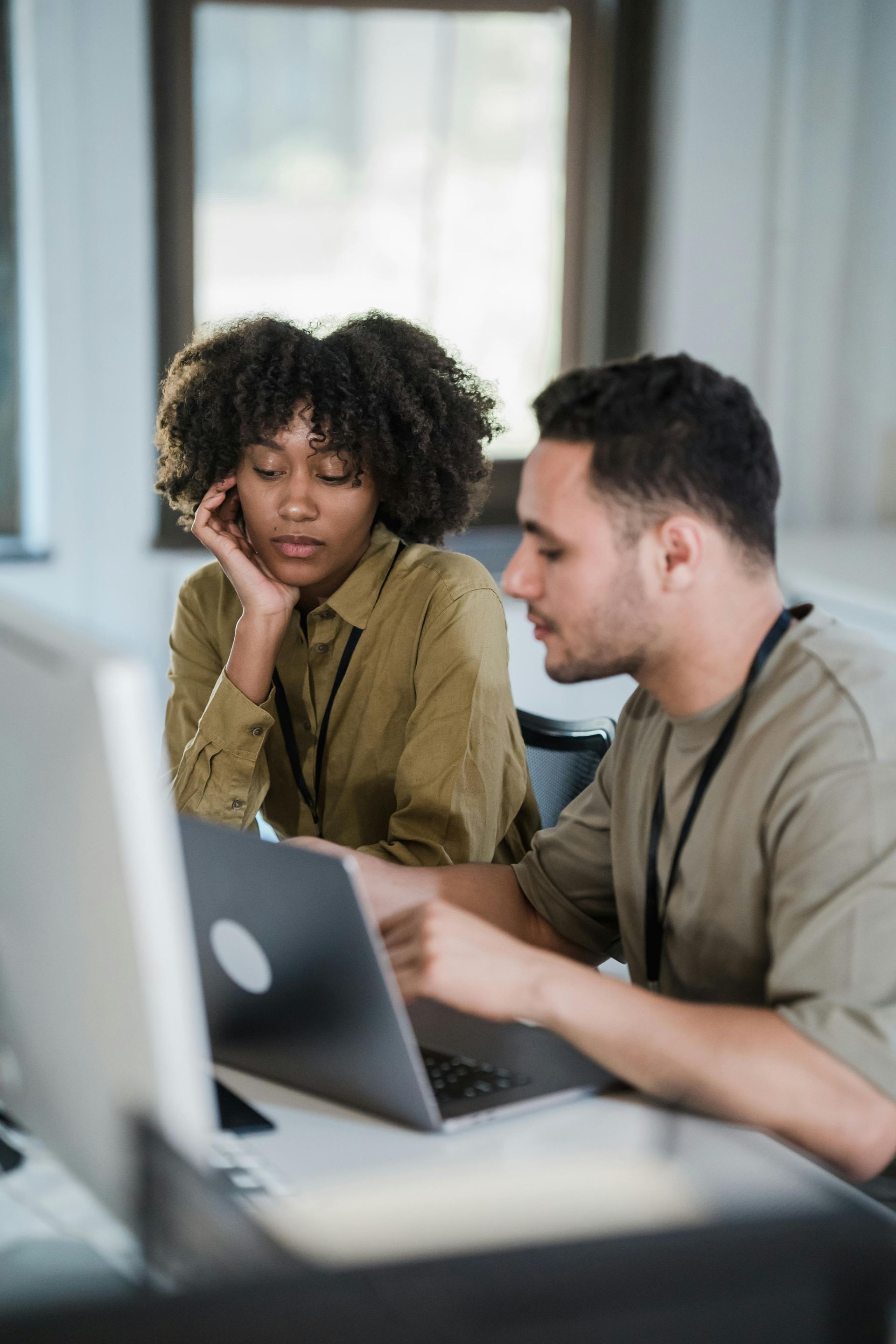 Two coworkers collaborating at a laptop in a bright office, one pointing at the screen