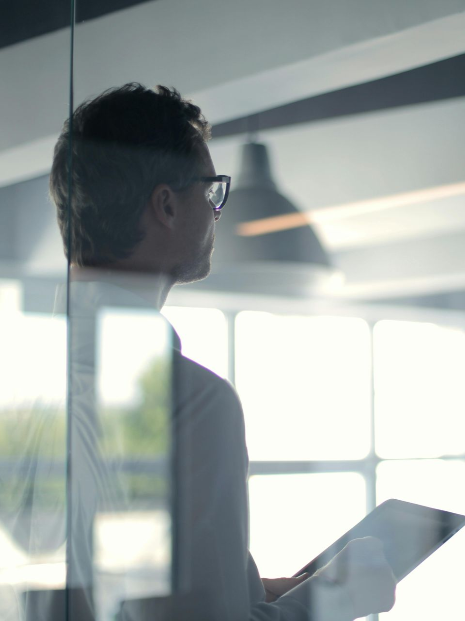 Person in glasses holding a tablet near a bright office window