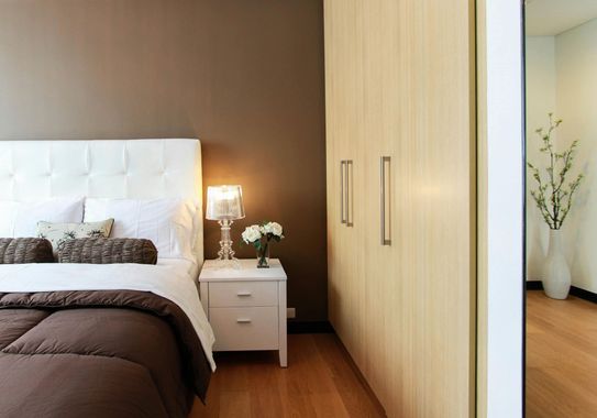 Modern bedroom with white bed, bedside lamp, and light wood wardrobe with mirror