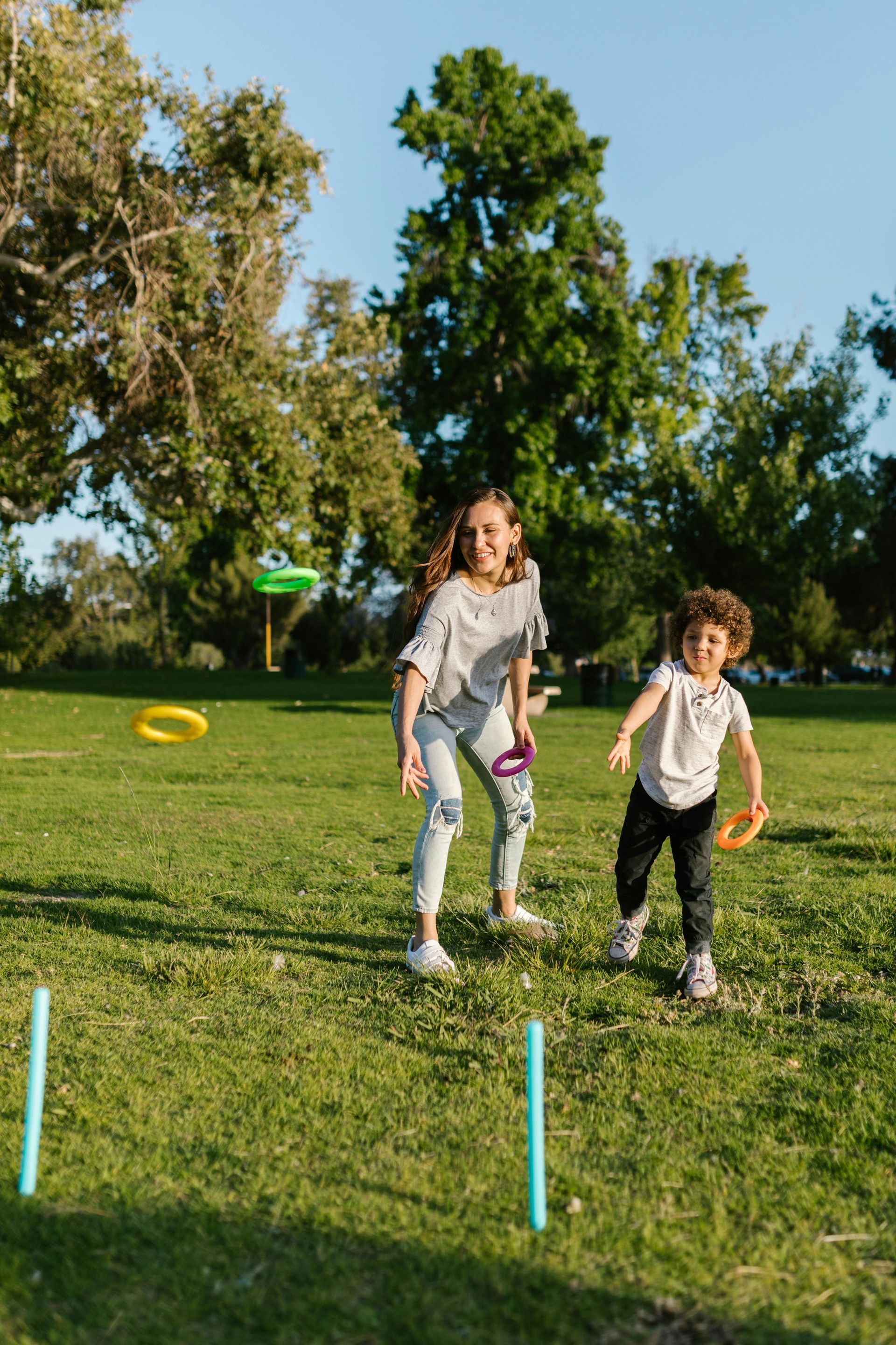 Two children running on a grassy field toward colorful flying discs under a clear blue sky