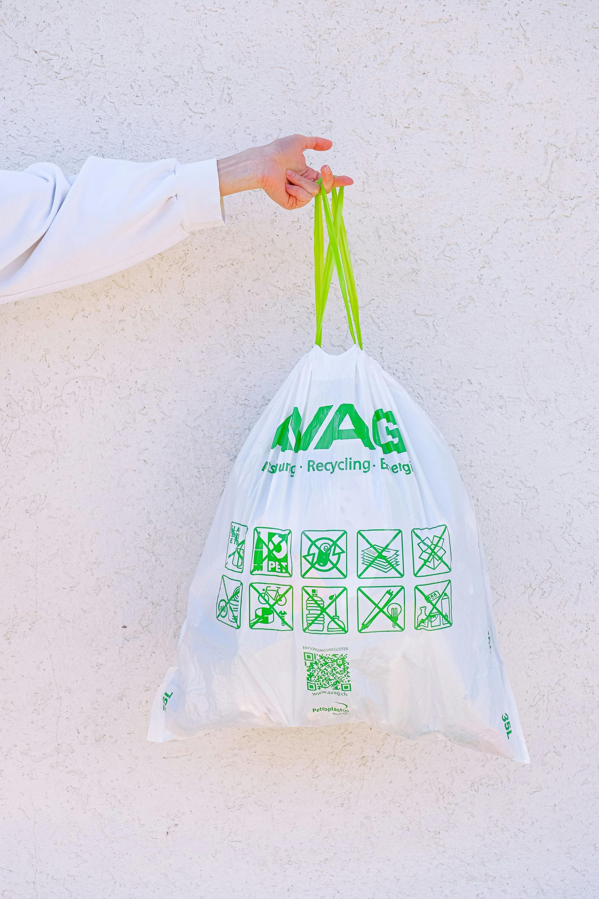 Hand holding a white shopping bag with green handles and green logo against a light wall
