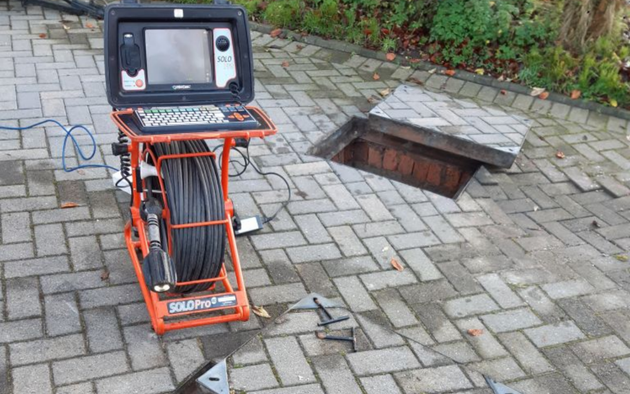 Drain inspection camera next to an open drain manhole on a block paving drive.