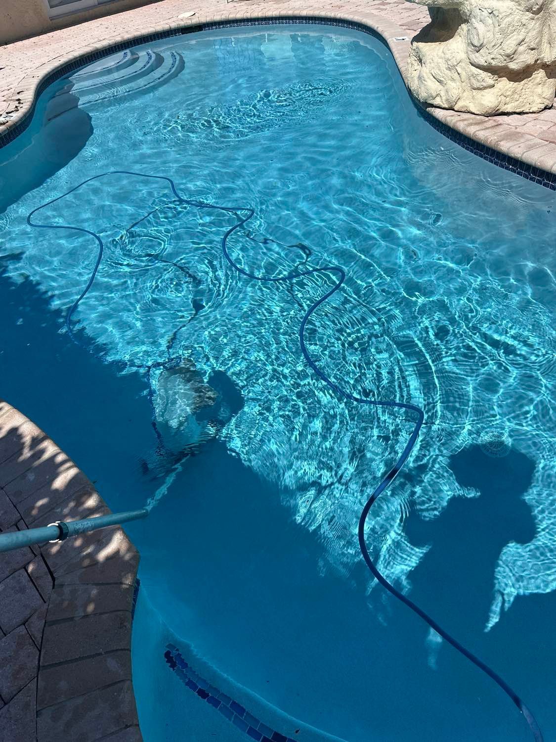 Blue pool with steps and a hose being used for cleaning.