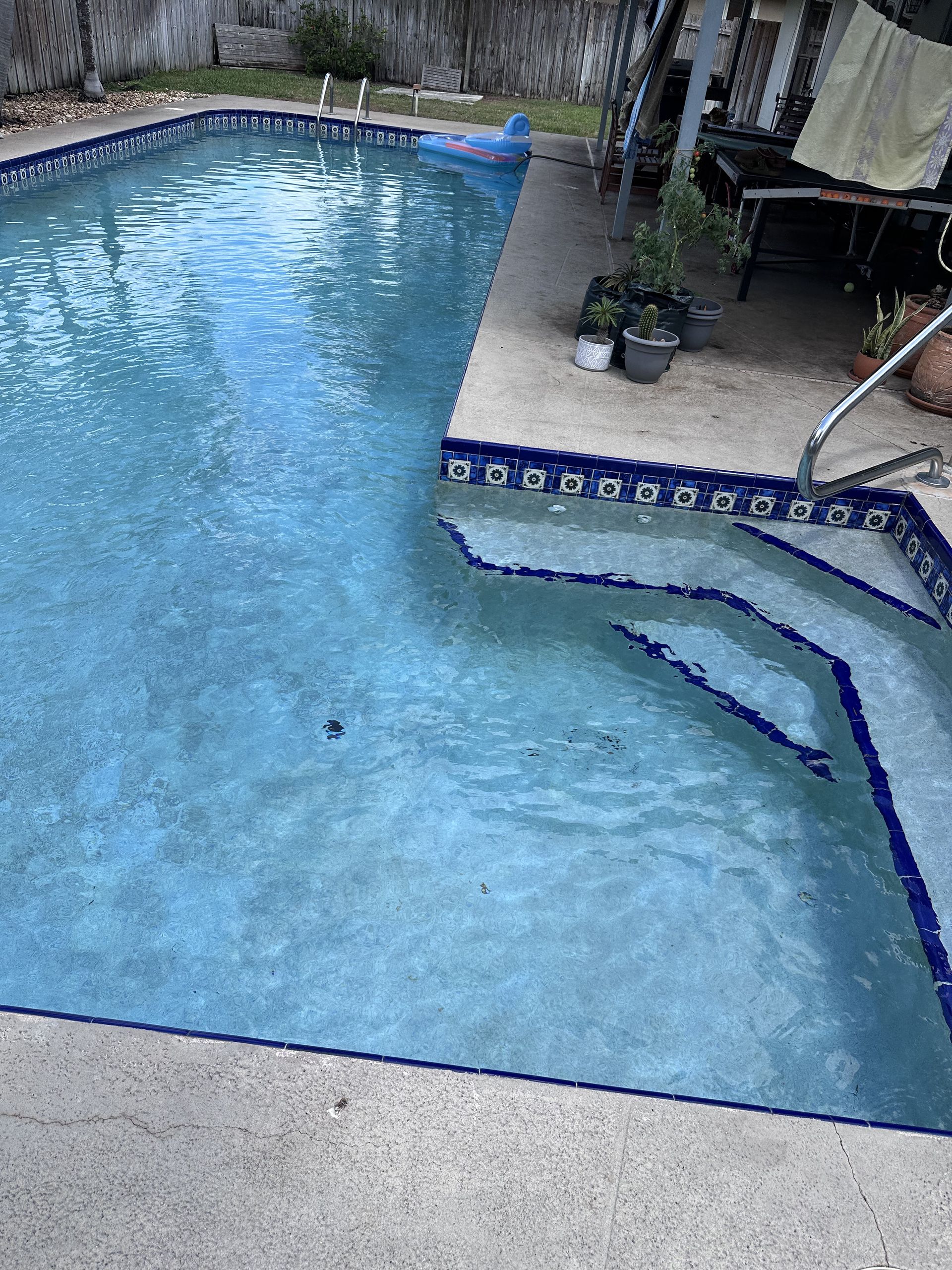 A swimming pool with blue water and steps. Concrete deck and blue tile trim.