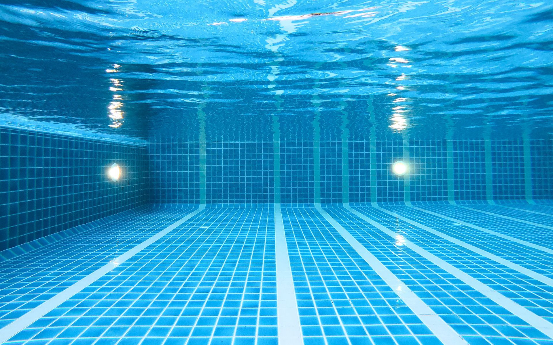 Underwater view of a tiled swimming pool with two lights illuminating the walls and floor.