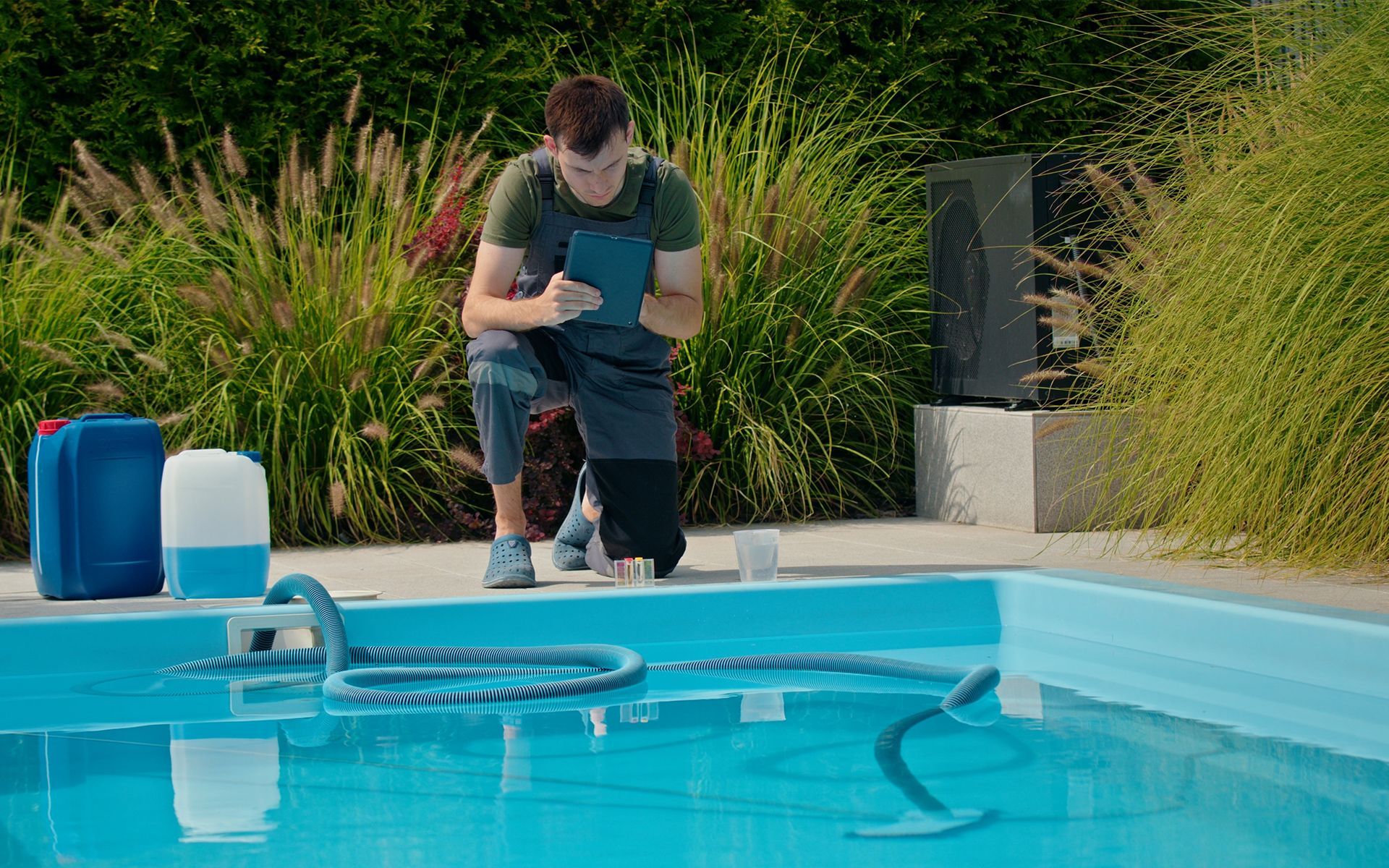 Man kneeling by a swimming pool, taking notes; cleaning supplies and cleaner visible.