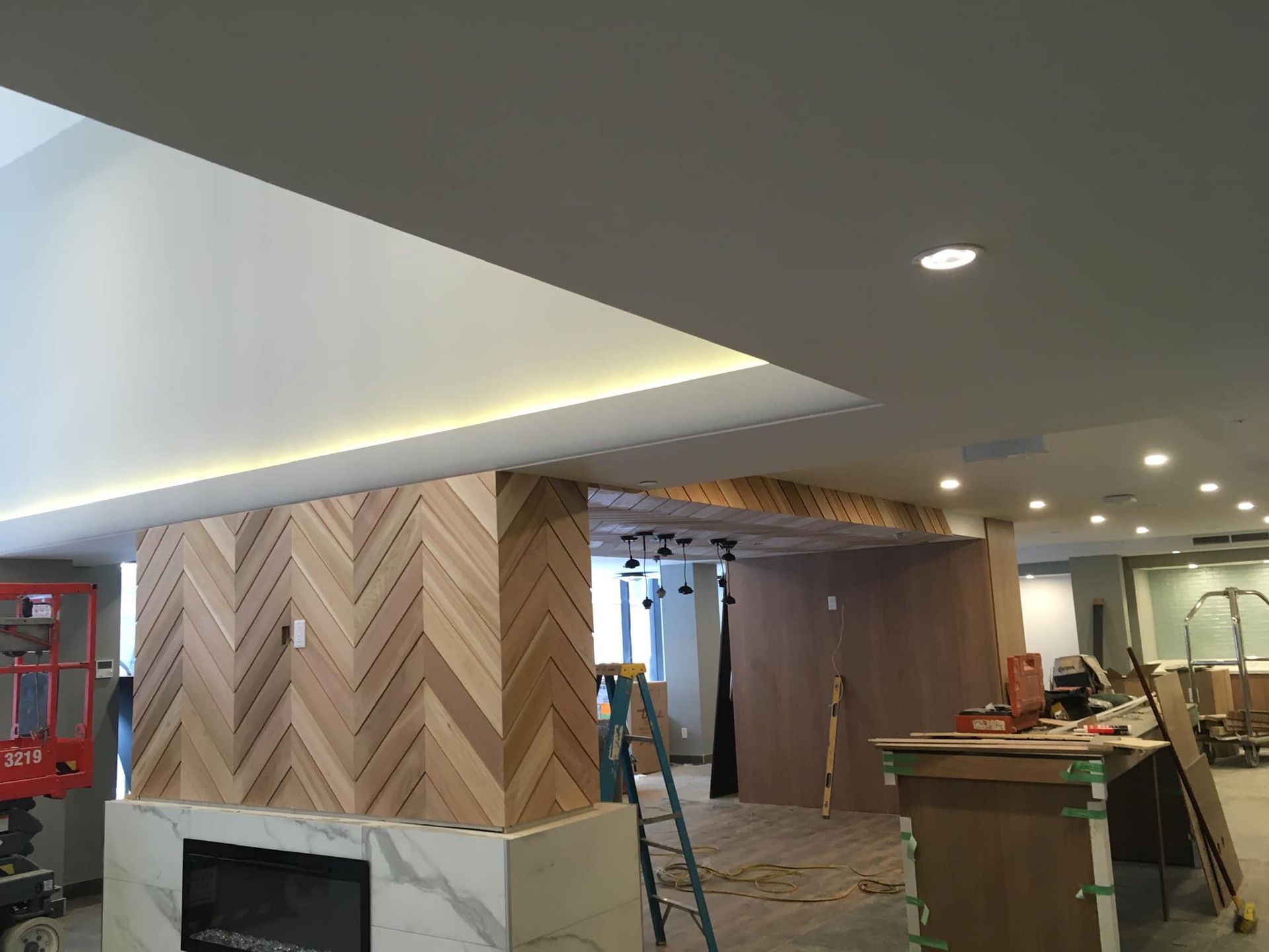 Hall d'entrée en construction avec lambris en bois à chevrons, éclairage au plafond et échelles dans un intérieur inachevé.