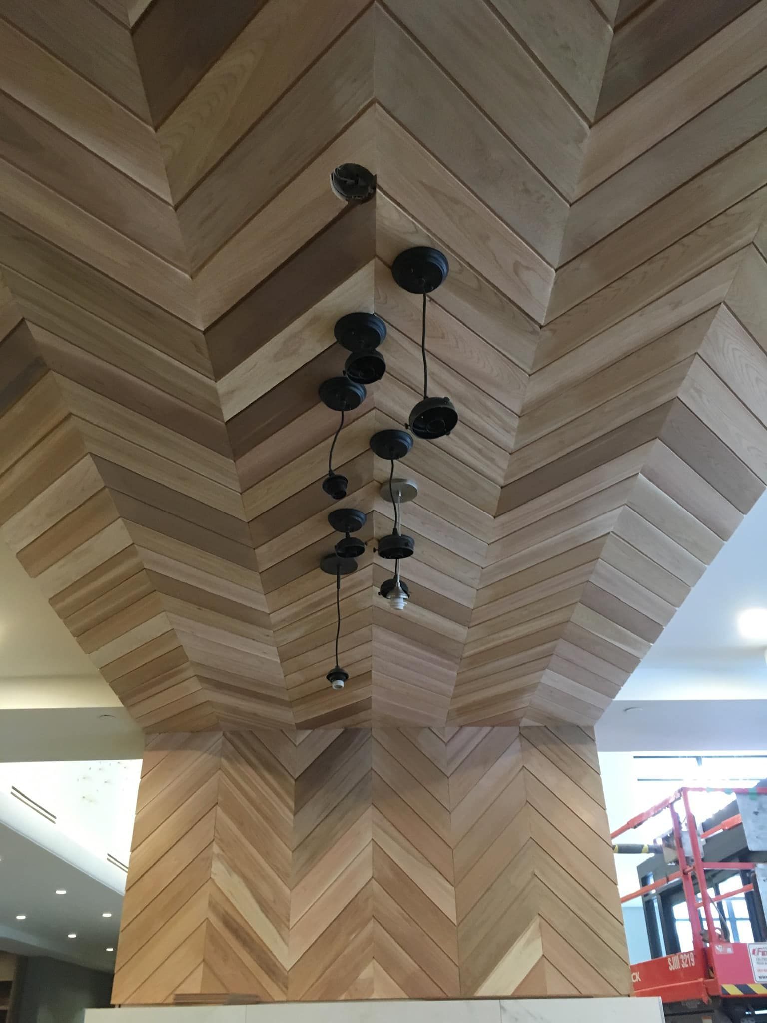 Plafond en bois à chevrons avec un ensemble de suspensions lumineuses noires dans un intérieur moderne.