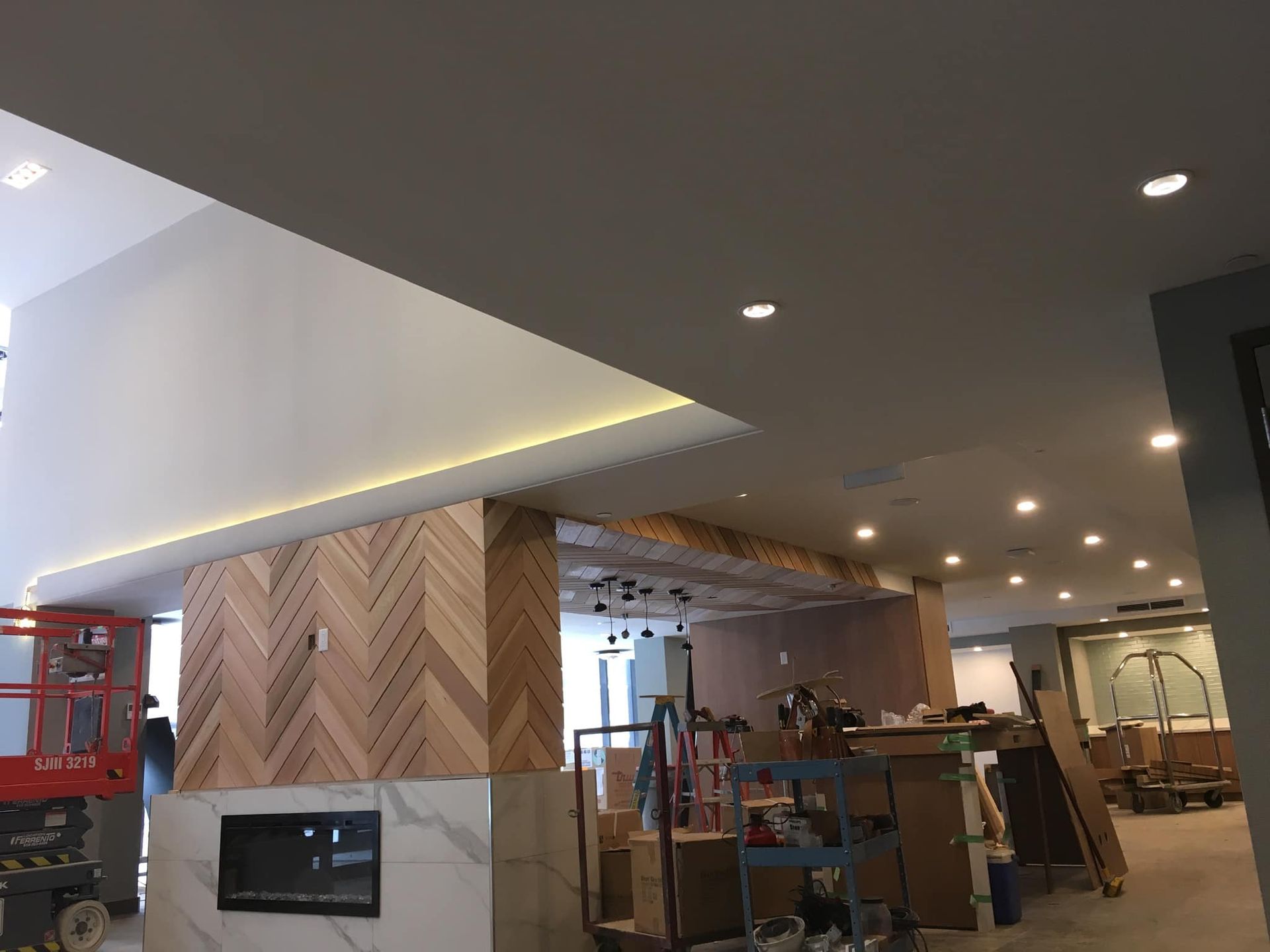 Intérieur moderne en cours d'aménagement avec murs lambrissés, éclairage encastré, échafaudages et outils.
