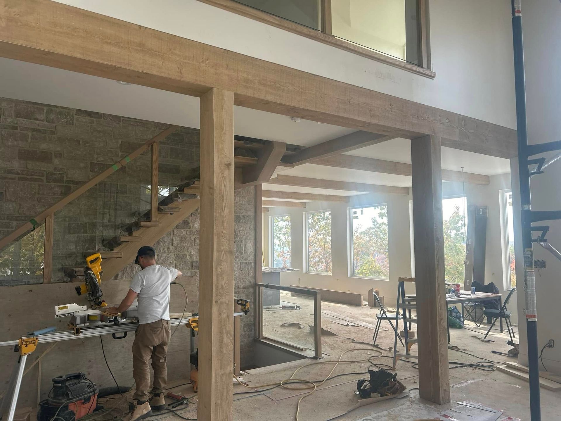 Un ouvrier du bâtiment utilise une scie à onglet dans une pièce spacieuse et inachevée, aux briques apparentes et aux poutres en bois.