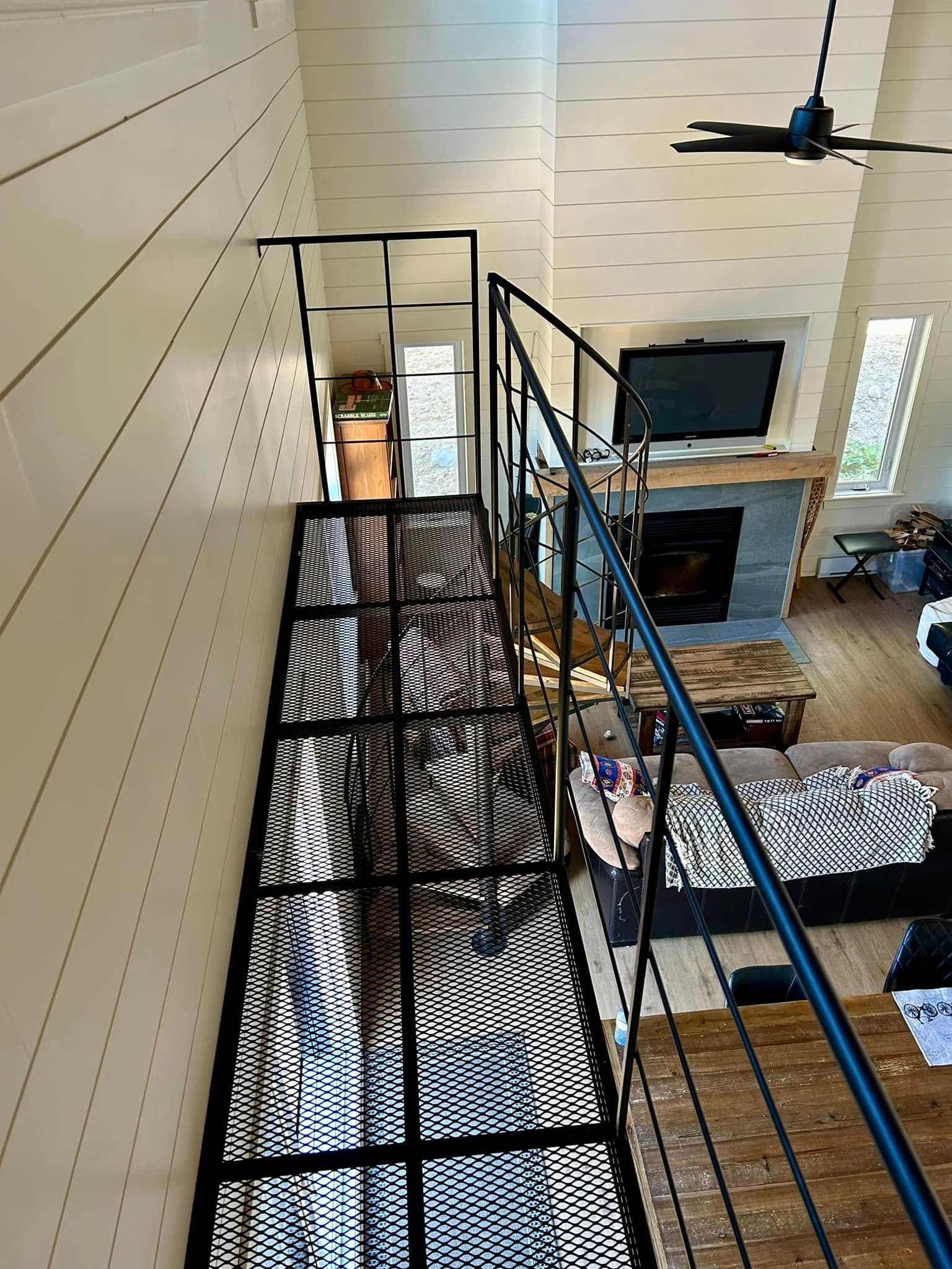 Passerelle métallique noire surélevée au-dessus d'un salon avec rambardes bleues et ventilateur de plafond