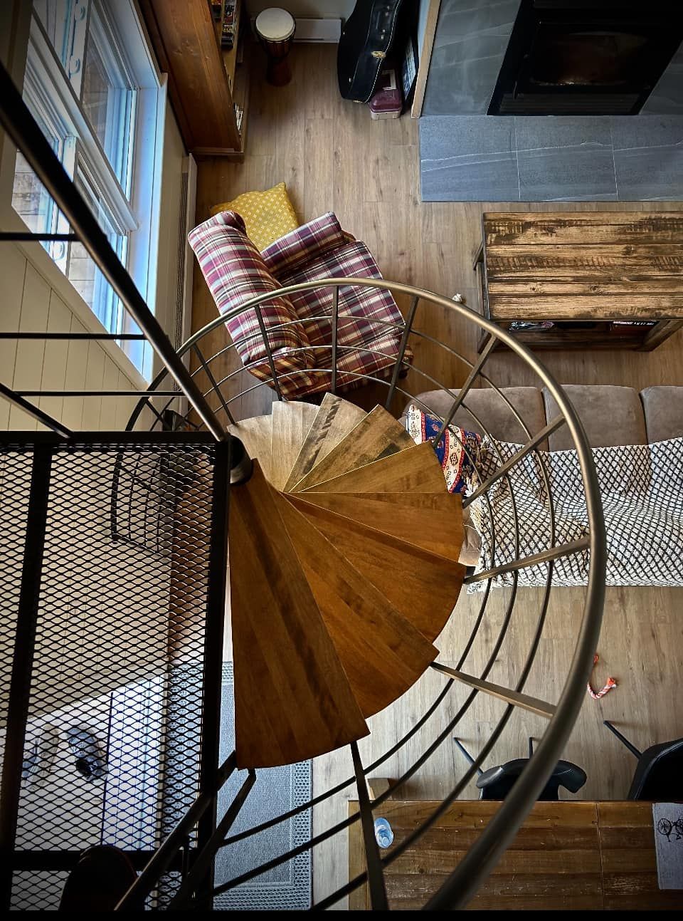 Vue de dessus d'un escalier en colimaçon incurvé avec une rampe en bois et des tapis à motifs en dessous.