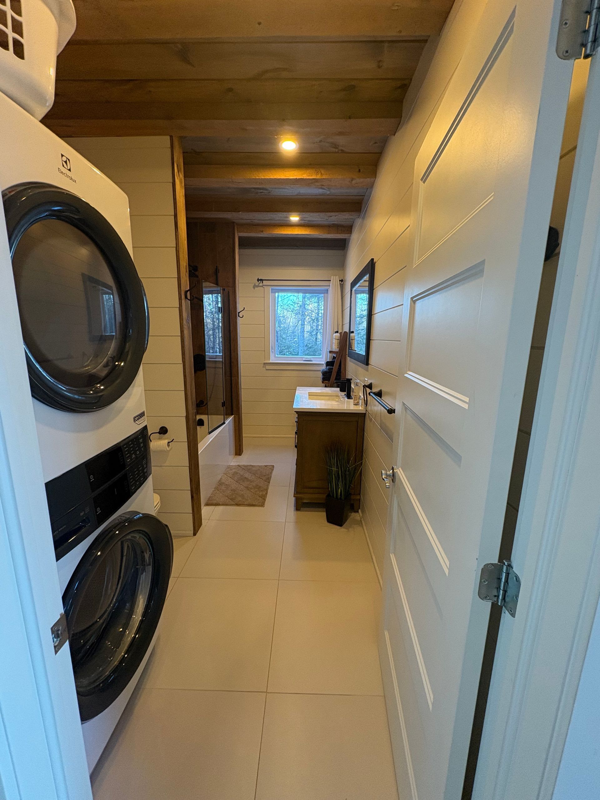 Couloir étroit donnant sur la buanderie, avec lave-linge et sèche-linge superposés sur la gauche et une salle de bains au fond.