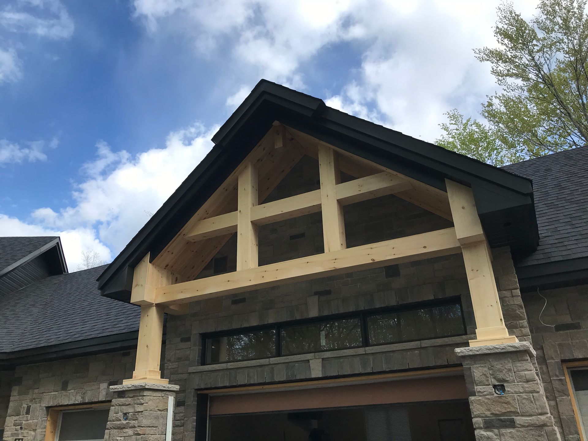 Extérieur d'une maison avec des piliers en pierre, des ornements de pignon en bois et un ciel nuageux