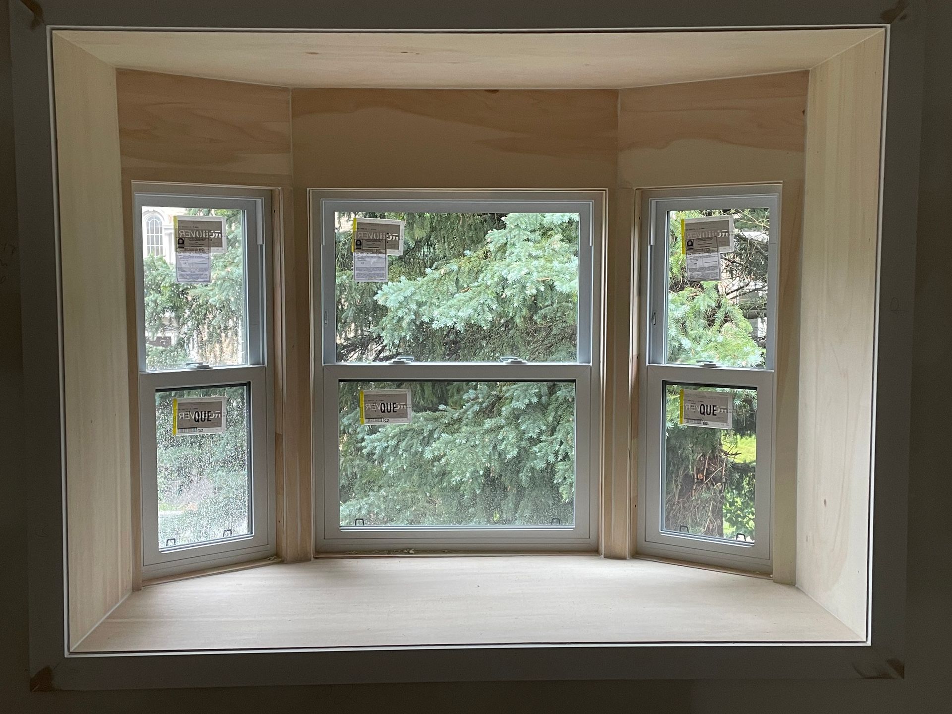 Fenêtre en baie vitrée à plusieurs carreaux donnant sur les arbres et la végétation luxuriante à l'extérieur.