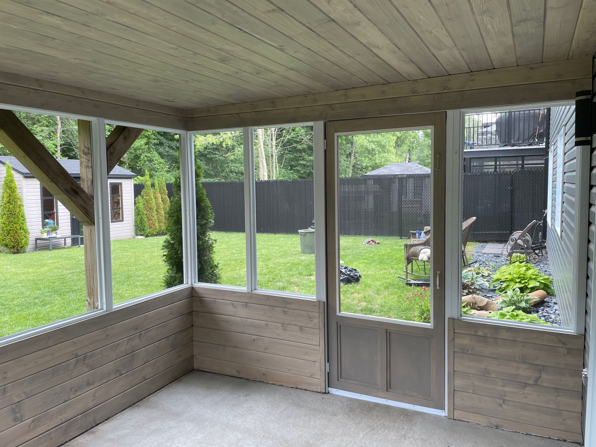 Terrasse couverte donnant sur un jardin arrière verdoyant avec porte moustiquaire et espace jardin clôturé.