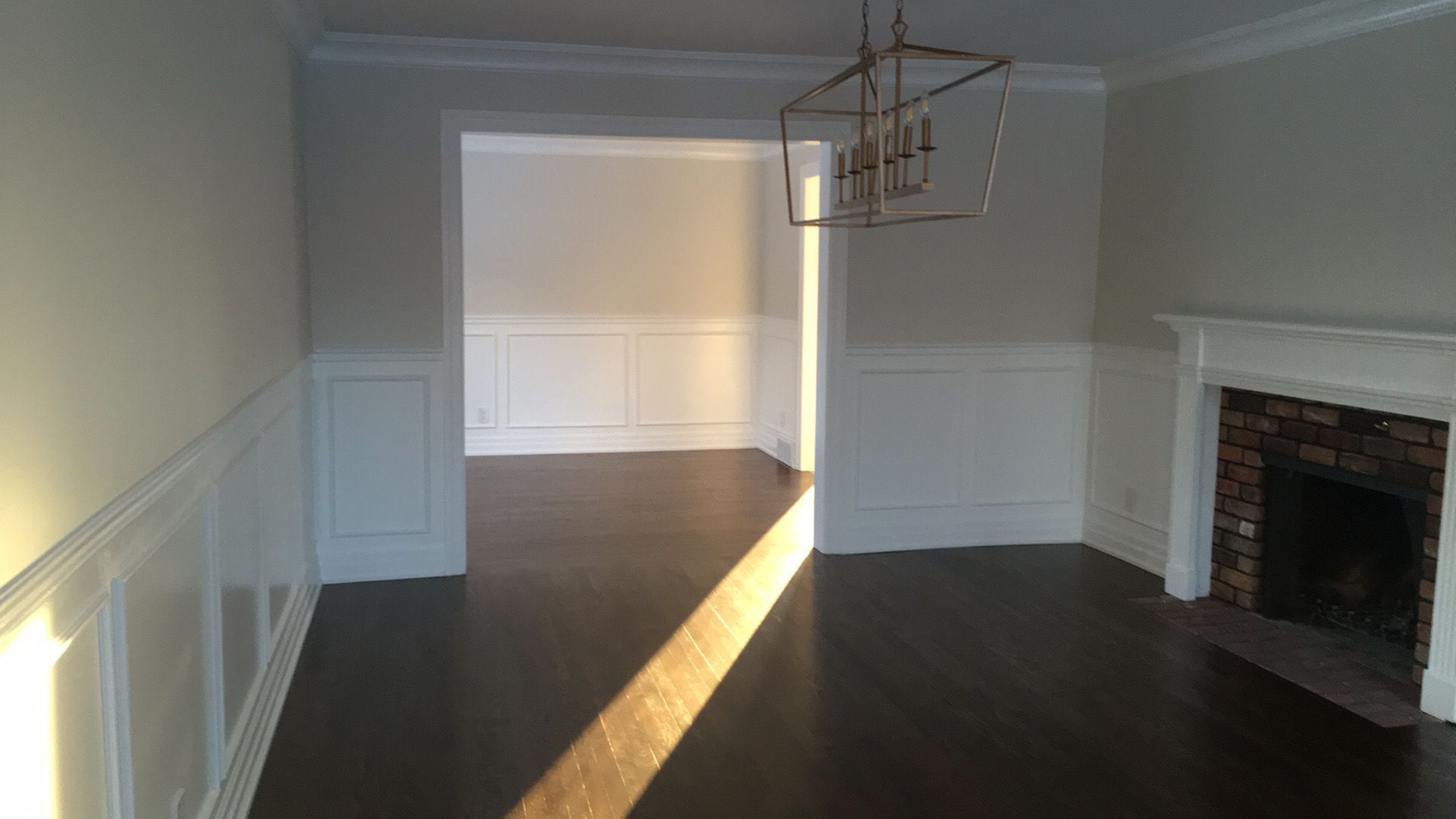 Salle à manger vide avec parquet foncé, lambris blancs, cheminée et lumière du soleil inondant le sol