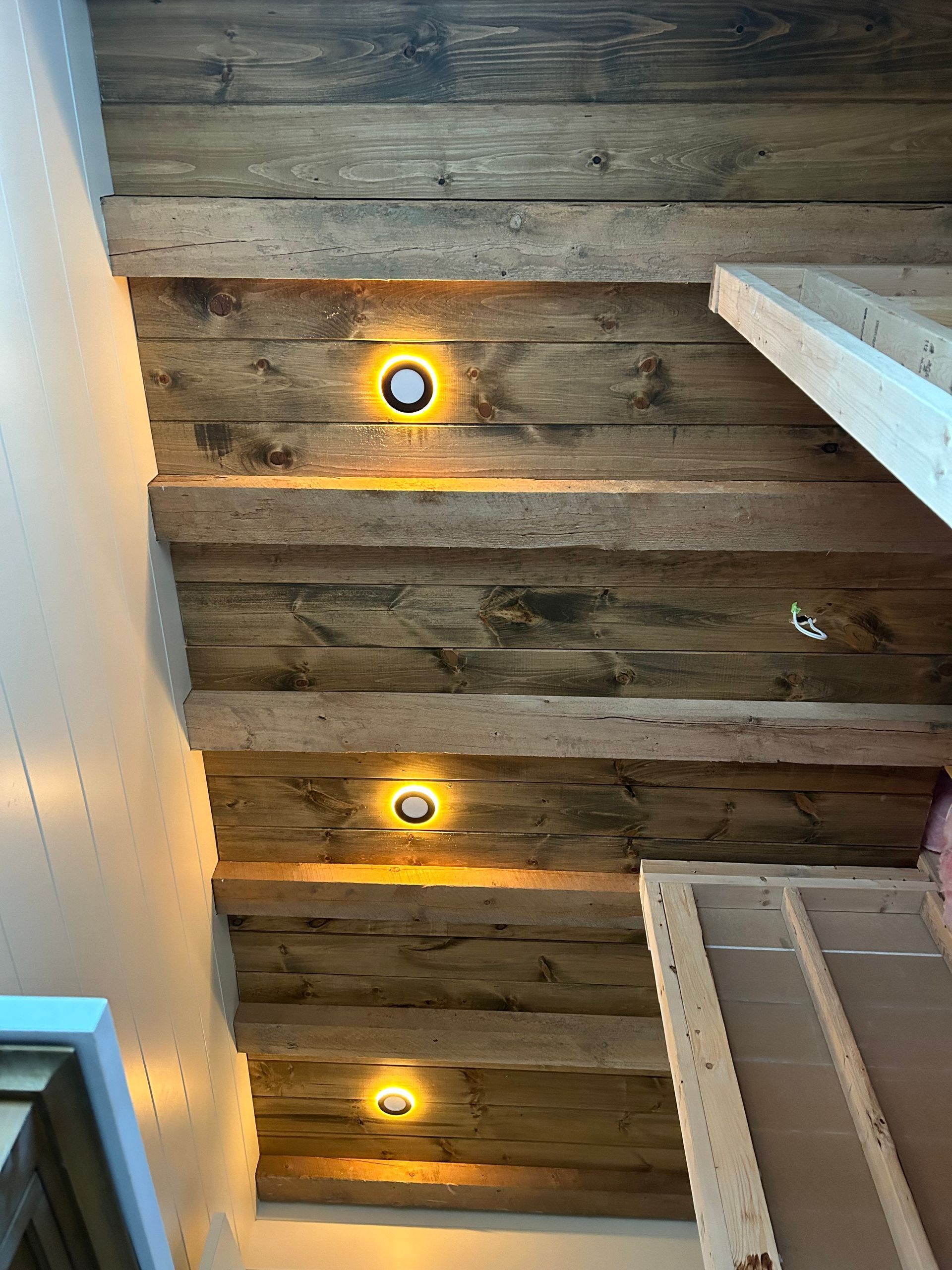 Plafond rustique à poutres apparentes avec trois petits spots encastrés jaunes et un bord de mur blanc