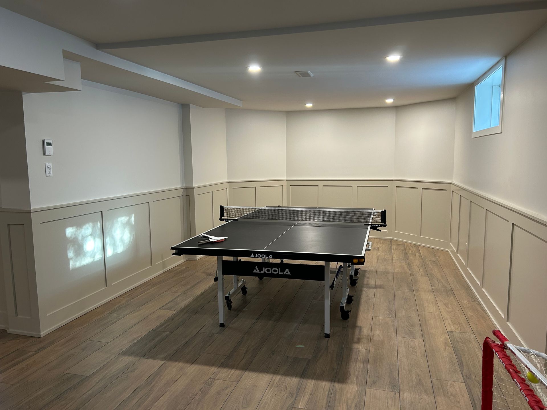 Pièce au sous-sol avec une table de ping-pong placée au centre, sous des spots encastrés et des murs lambrissés.
