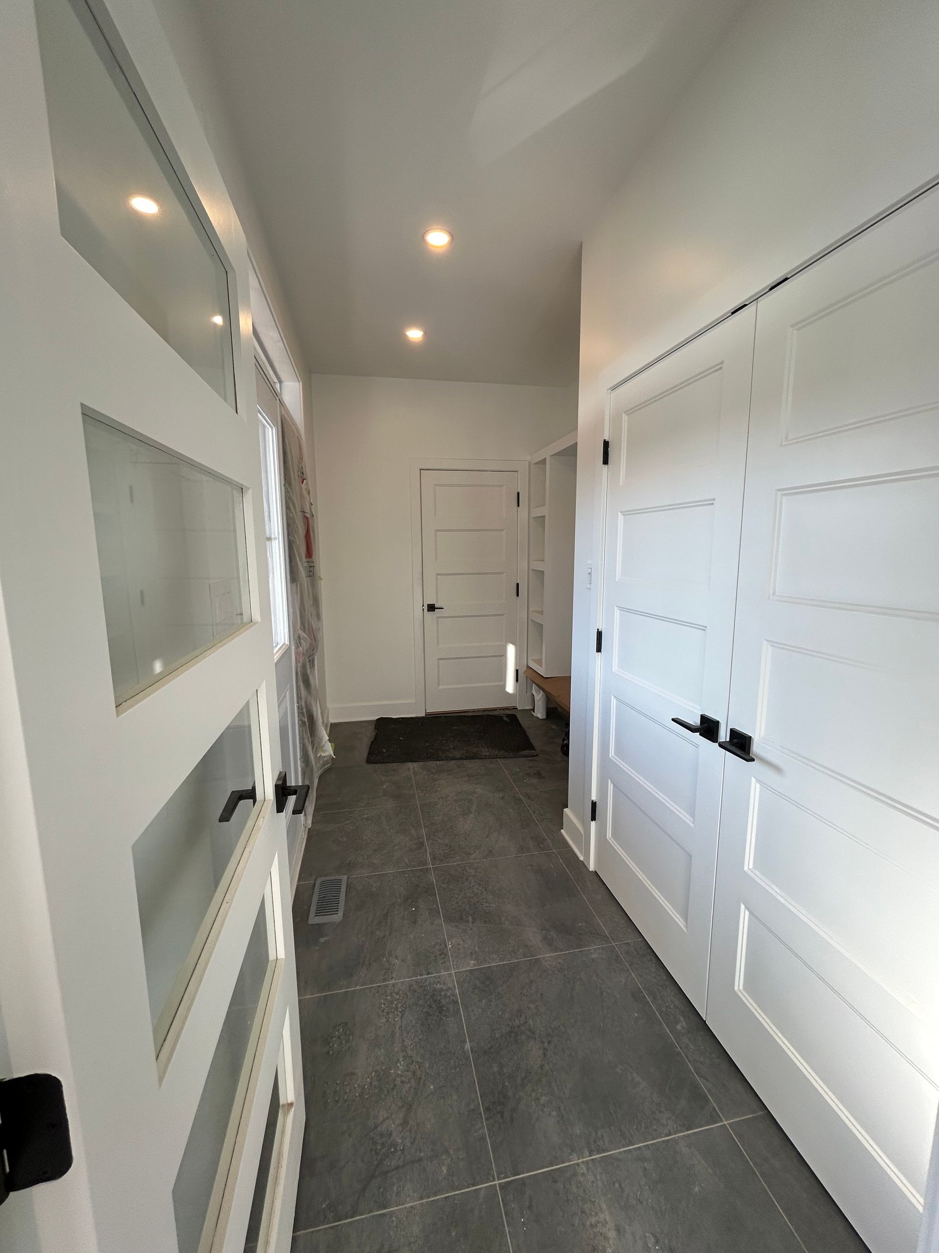 Couloir blanc moderne avec placards intégrés, éclairage encastré et sol carrelé gris.