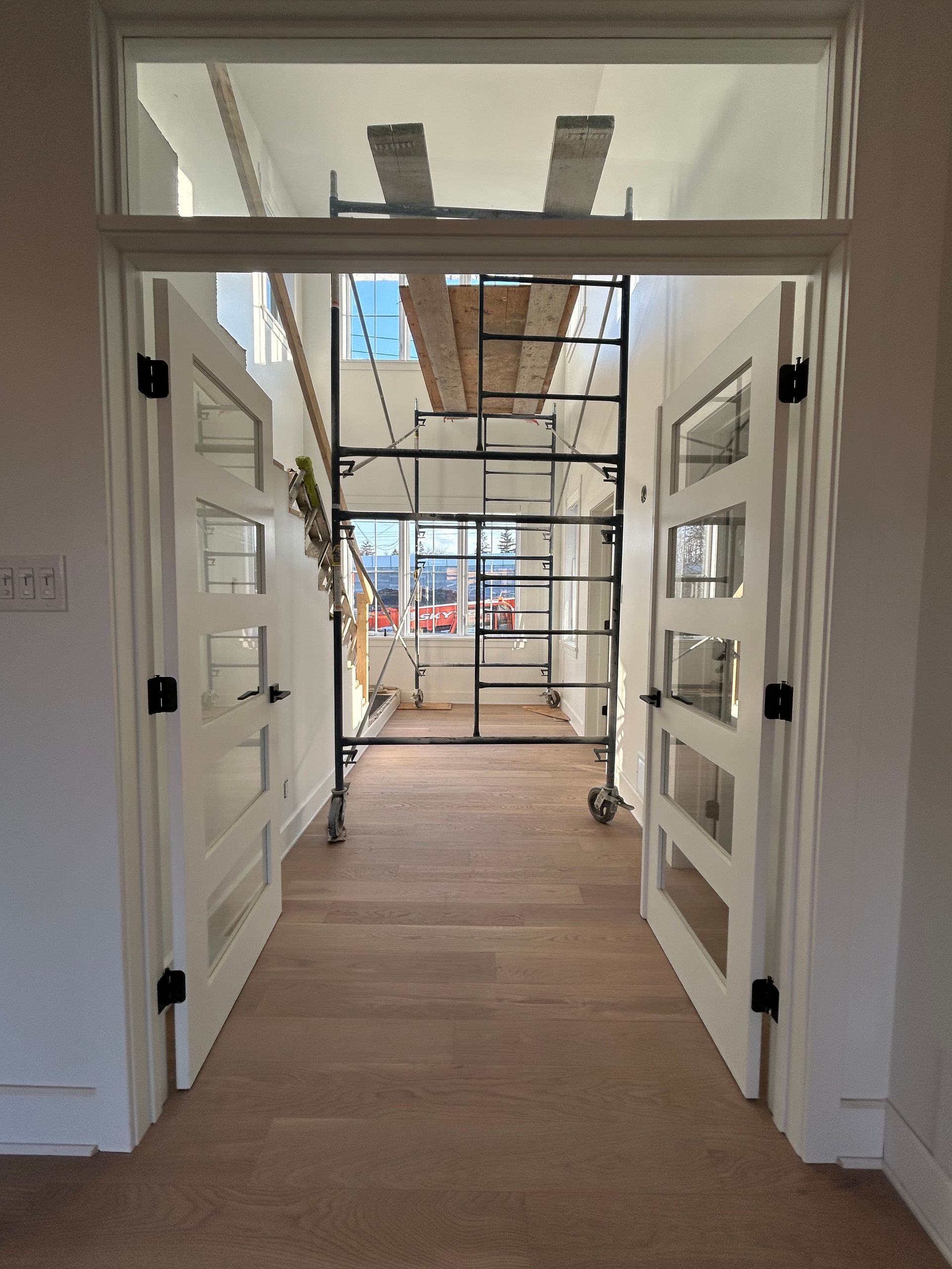 Couloir intérieur en rénovation avec échafaudages et vue sur l'extérieur à travers des portes doubles ouvertes