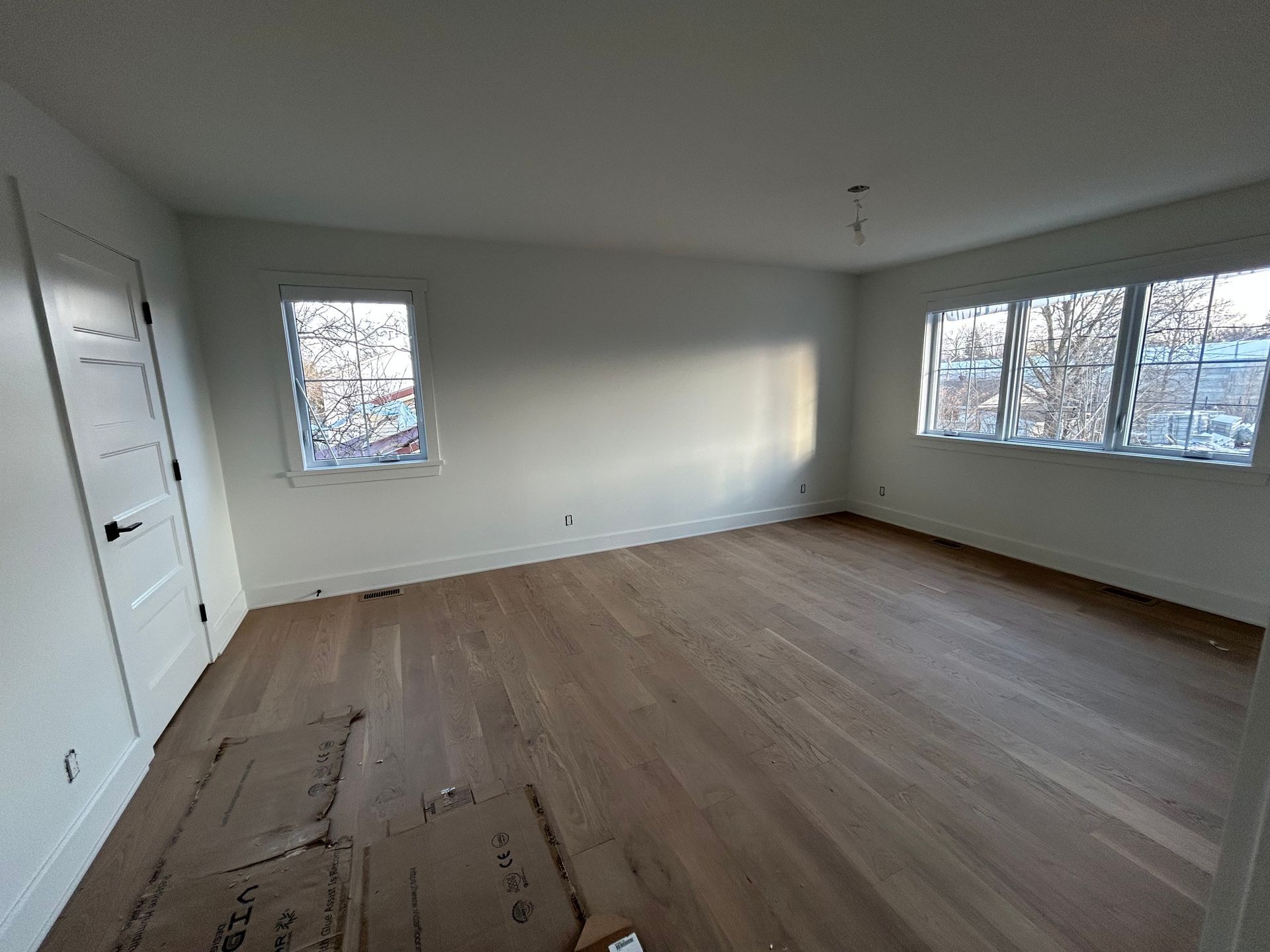 Chambre vide non meublée avec murs blancs, parquet et trois fenêtres laissant entrer la lumière du jour